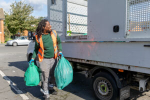 A member of the street cleaning team puts full litter bags in the back of a collection vehicle.