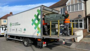 Two members of the bulky waste collections team lift a sofa into the back of a collection vehicle.