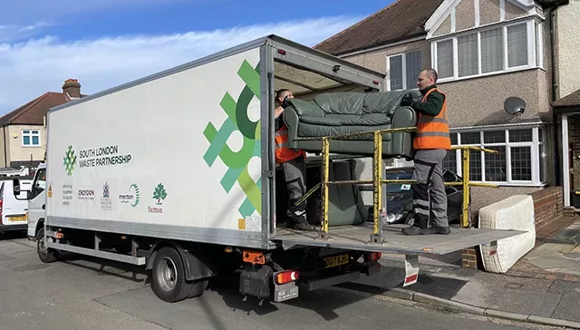 Two members of Veolia's bulky waste collection team load a sofa onto the back of a collection vehicle.