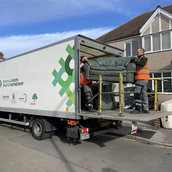Two members of the bulky waste collections team load a sofa into the back of a collection vehicle.