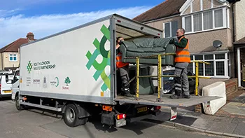 Two members of the bulky waste collection team lift a sofa into the back of a collection vehicle.