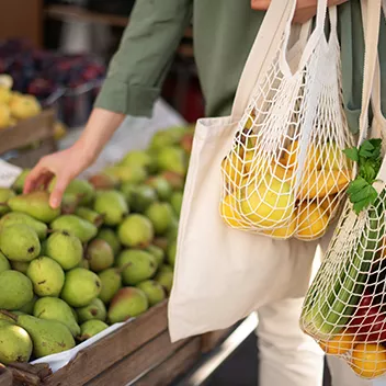 A shopper putting fruit in a reusable net bag.