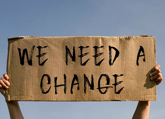 Image of someone holding up a sign that has the words 'we need change' on it.