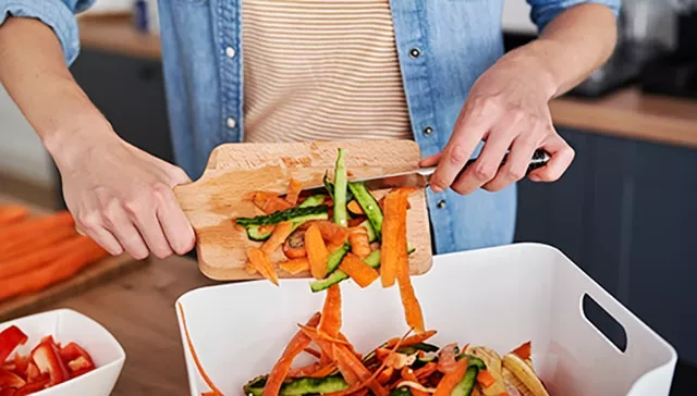 Image of a person scraping vegetable peeling into a food waste bin.